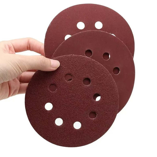 Hand holding three 125mm sanding discs with holes, showcasing their multi-grit aluminum oxide finish.