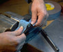 Hands using 600 grit emery cloth roll in a vise for precise sanding on metal surfaces.